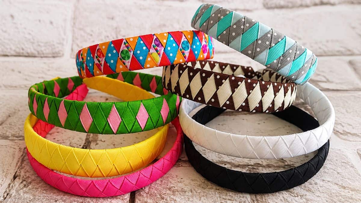 Colorful woven ribbon headbands in assorted patterns and solid colors displayed in a stacked arrangement on a textured surface.