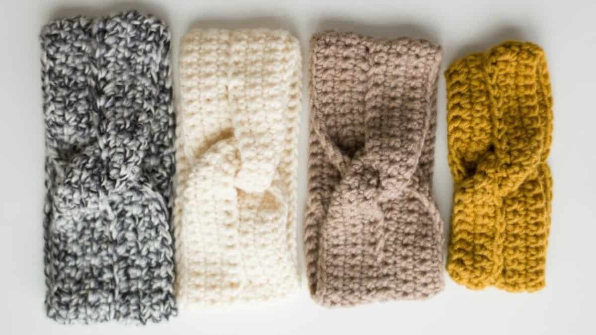 Four crocheted twist headbands in gray, cream, taupe, and mustard yarn displayed side by side on a white background.