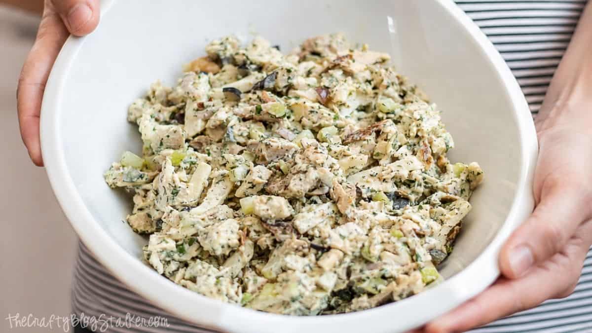 Creamy rotisserie chicken salad with chopped chicken, celery, onions, herbs, and dressing served in a large white mixing bowl held in both hands.