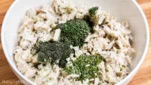 Rotisserie chicken salad ingredients in a white bowl topped with fresh parsley, dill, chives, and minced garlic before mixing.
