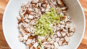 Chopped rotisserie chicken and diced celery in a white mixing bowl, ready to be mixed into a homemade chicken salad.