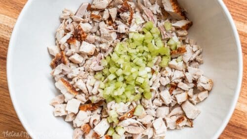 Chopped rotisserie chicken and diced celery in a white mixing bowl, ready to be mixed into a homemade chicken salad.