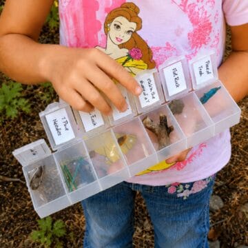 Child holding a clear pill box scavenger hunt game filled with collected outdoor items and labeled compartments.