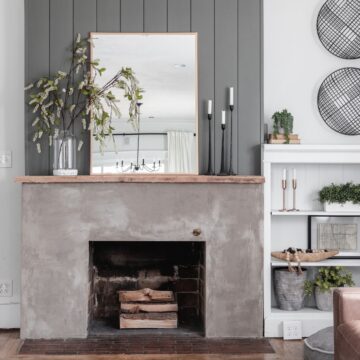 Modern concrete fireplace makeover with a rustic wood mantel, vertical shiplap accent wall, mirror, and minimalist decor in a bright living room.