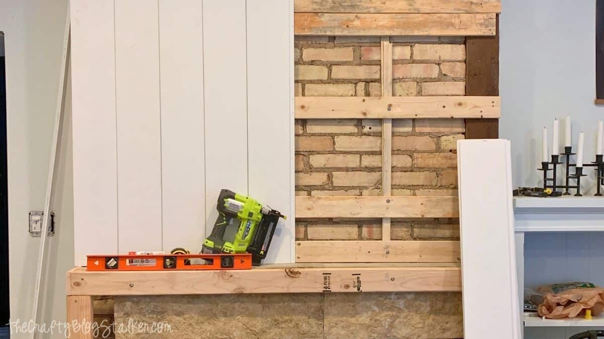 Wall framing and vertical shiplap being installed around a brick fireplace during a DIY fireplace makeover renovation.