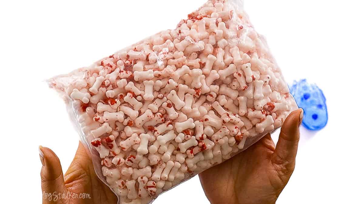 Hands holding a clear plastic bag filled with white bone-shaped candies splattered with red for a Halloween-themed treat.