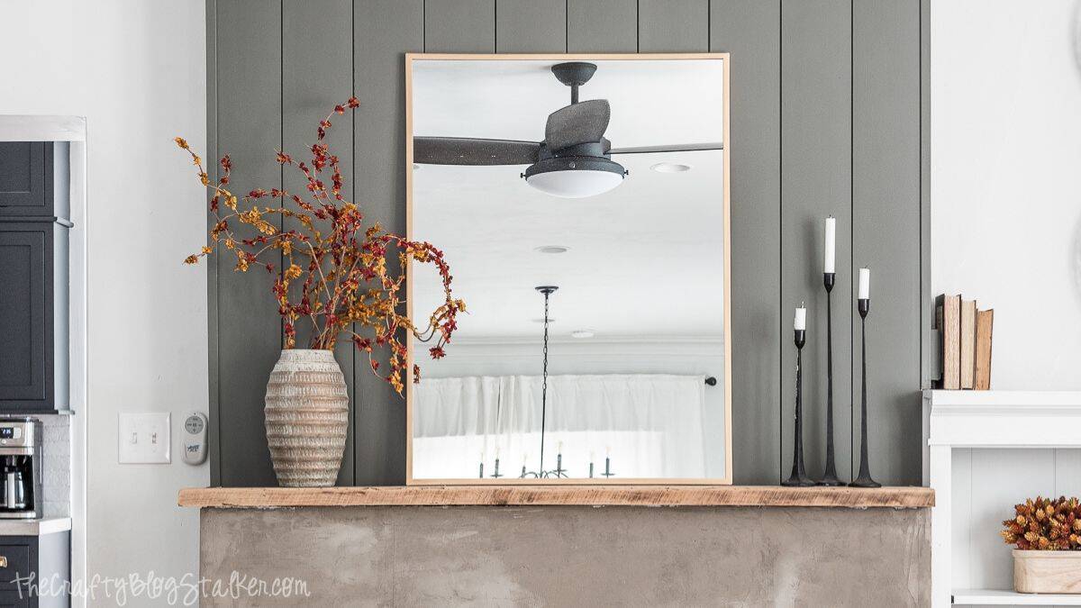 Simple fall mantel decorated with a large mirror, tall black candlesticks, and a textured vase filled with autumn branches.