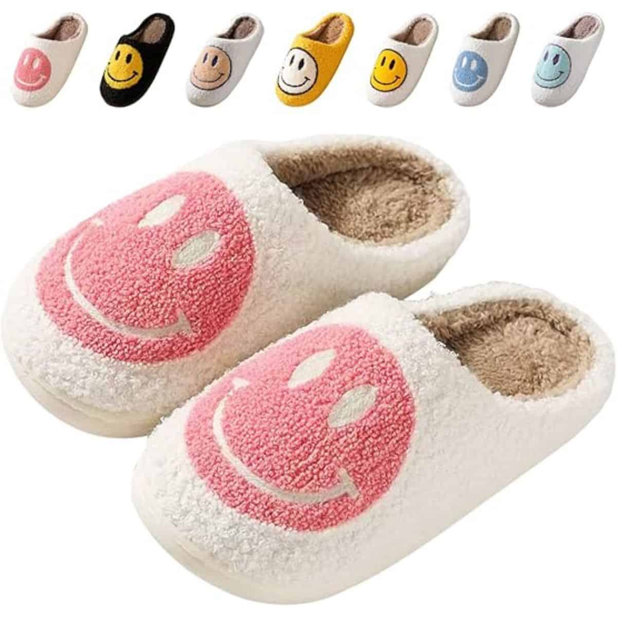 Pair of fuzzy white slippers with pink smiley faces on top, shown with additional color options including yellow, black, blue, and beige.