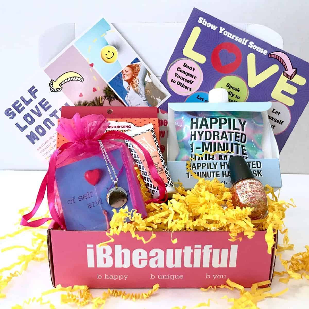 Pink iBbeautiful subscription box filled with self-love themed items including nail polish, face mask, necklace, and inspirational cards.