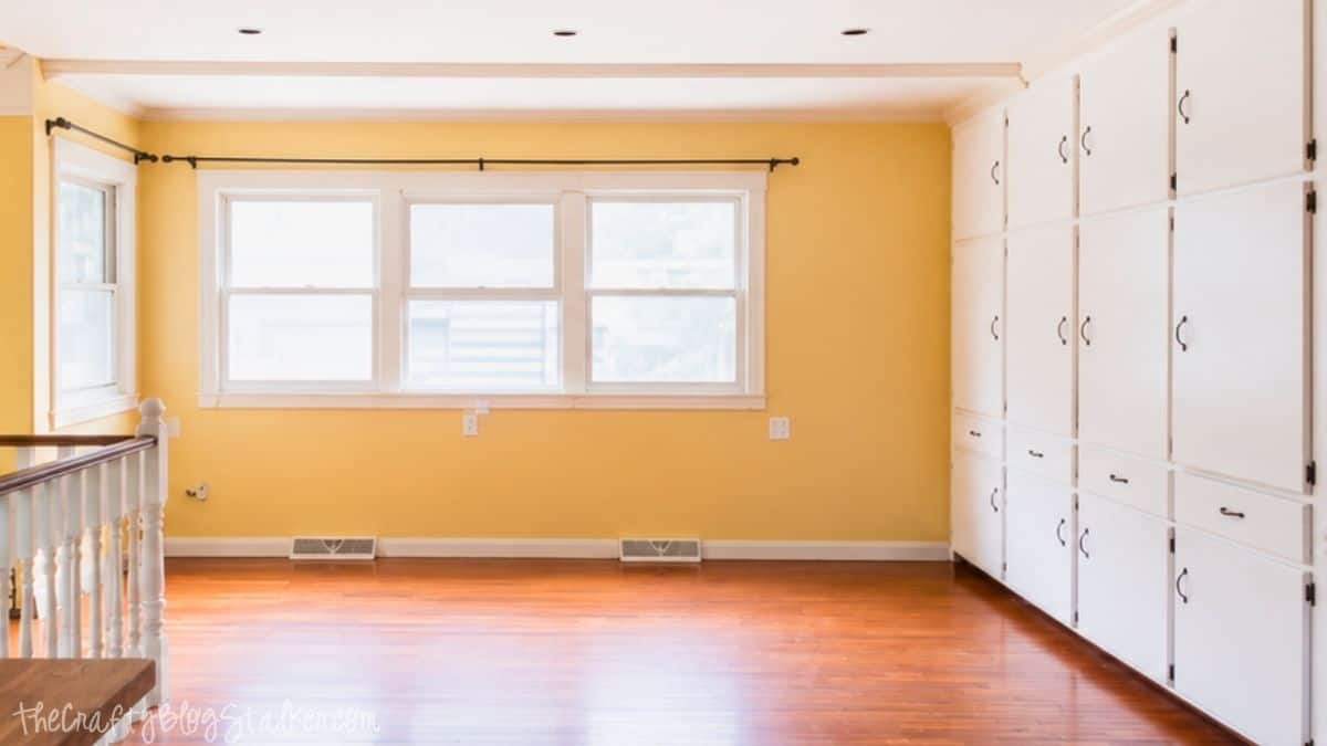 Empty dining room with yellow walls, hardwood floors, three large windows, built-in white storage cabinets, and natural light streaming inside.