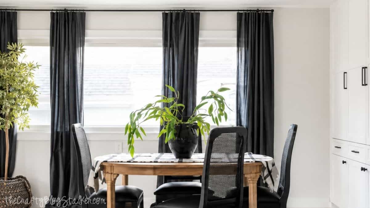 Dining room makeover with black floor-length curtains, a wood dining table, black chairs, white built-in cabinets, and a large potted plant.