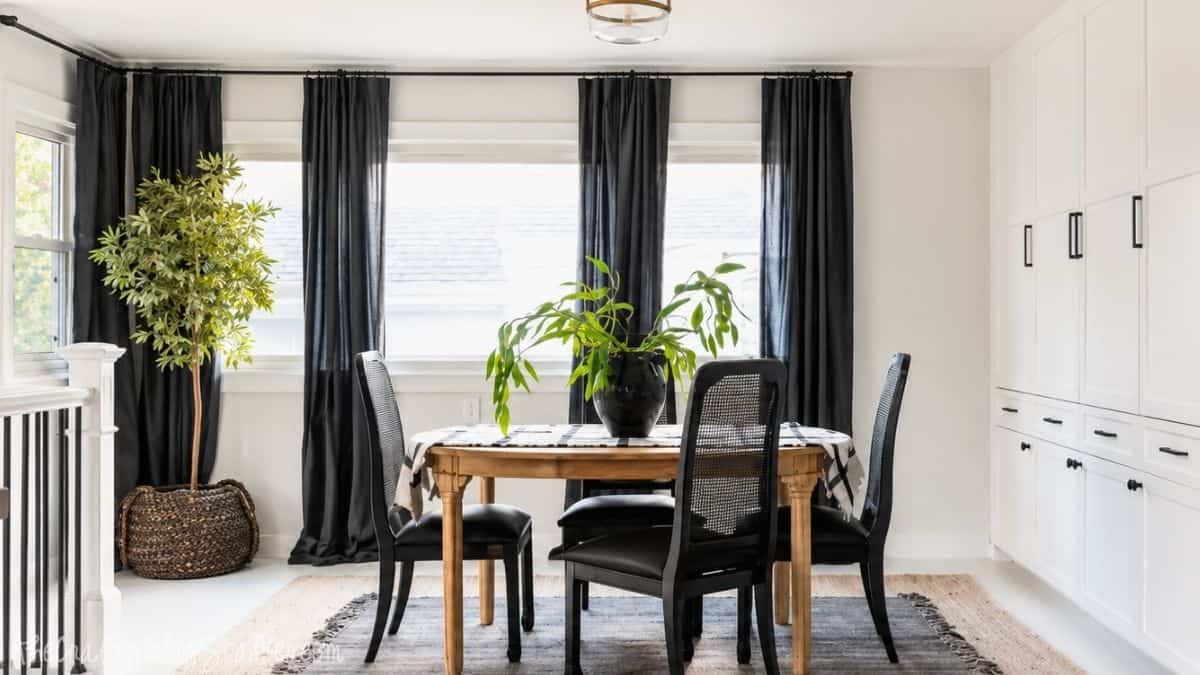 Modern dining room makeover with a wood table, black chairs, white built-in cabinets, black curtains, layered rugs, and indoor plants.