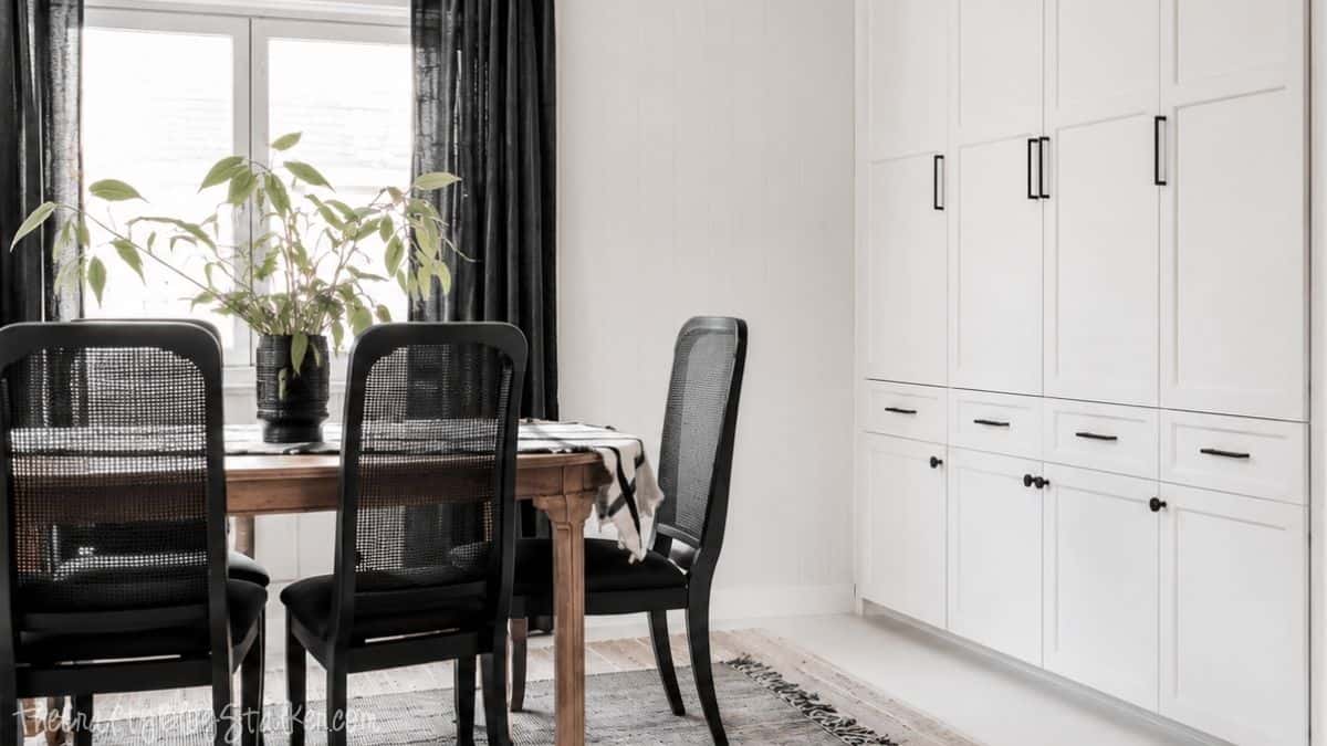 Updated dining room with white shaker-style cabinet doors, black hardware, a wood dining table, black chairs, and black curtains.