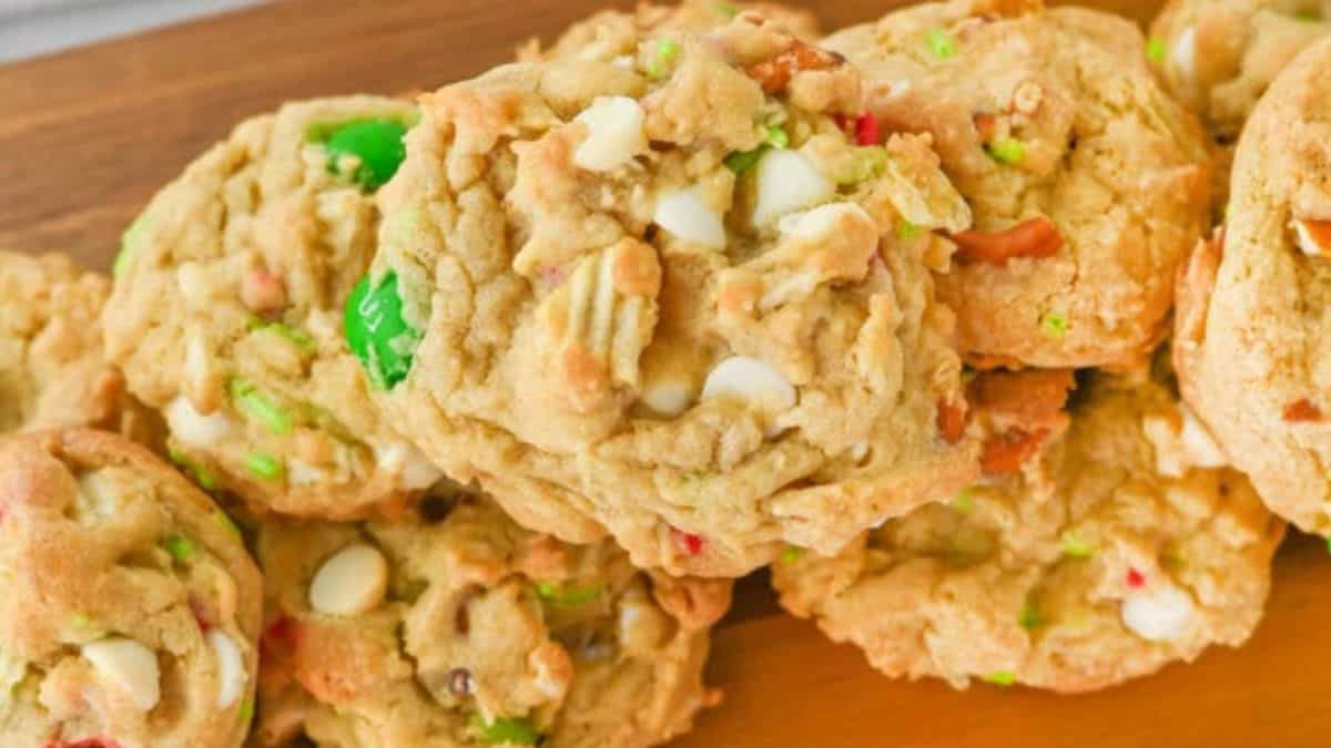 Stack of Christmas kitchen sink cookies filled with white chocolate chips, pretzel pieces, and red and green candy-coated chocolates on a wooden surface.
