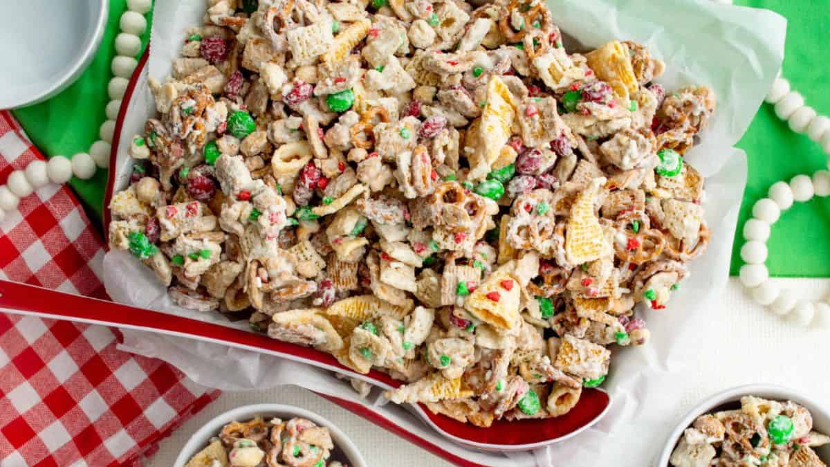 Tray of Christmas white chocolate Chex mix made with cereal, pretzels, peanuts, red and green M&Ms, and candy sprinkles, served with a red spoon.
