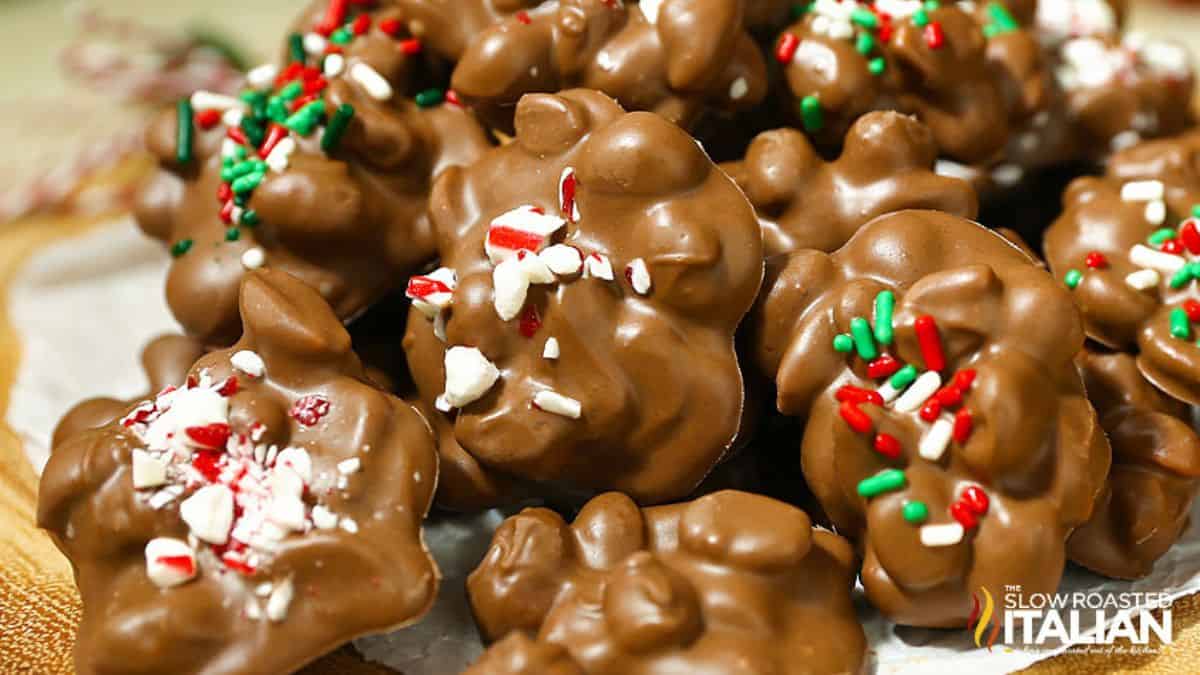 Pile of chocolate peanut clusters topped with crushed peppermint and red, green, and white sprinkles, displayed as festive holiday candy treats.