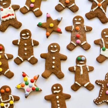 Gingerbread cookies shaped like people and stars decorated with white icing and colorful candy buttons on a white background.