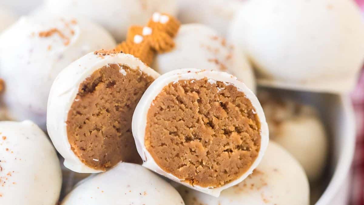 Close-up of gingersnap truffles coated in white chocolate, with one truffle cut open to show the soft spiced cookie filling inside.