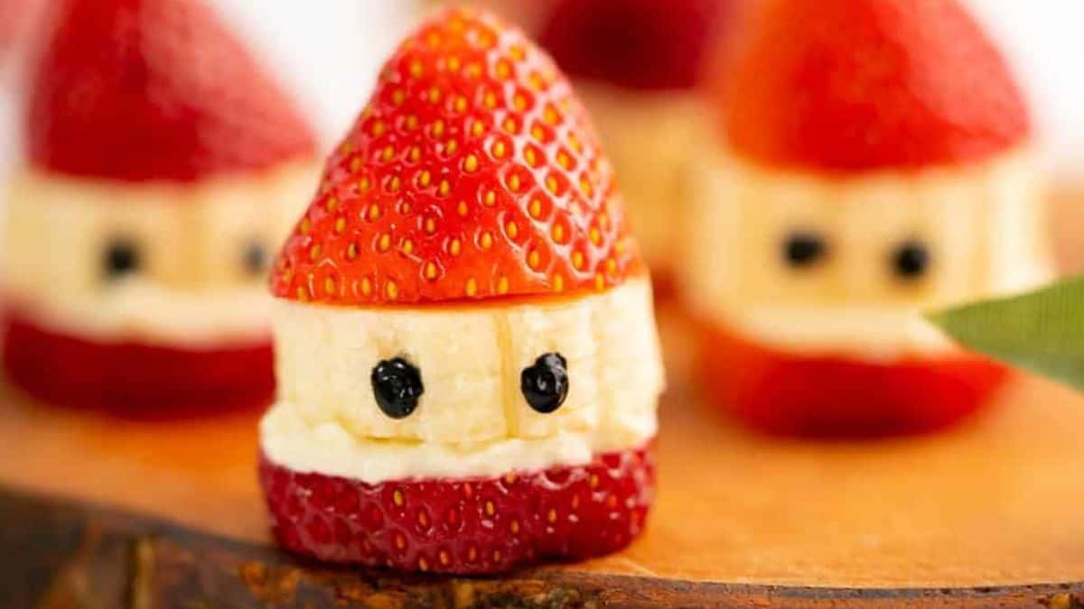 Close-up of a strawberry and banana Santa snack with chocolate eyes, made from fruit slices stacked to look like Santa's face and hat.