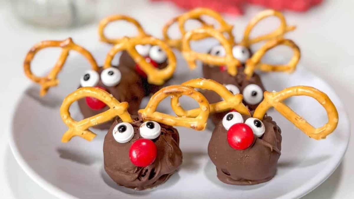 Chocolate reindeer treats made with pretzel antlers, candy eyes, and red candy noses arranged on a white plate for a festive holiday dessert.