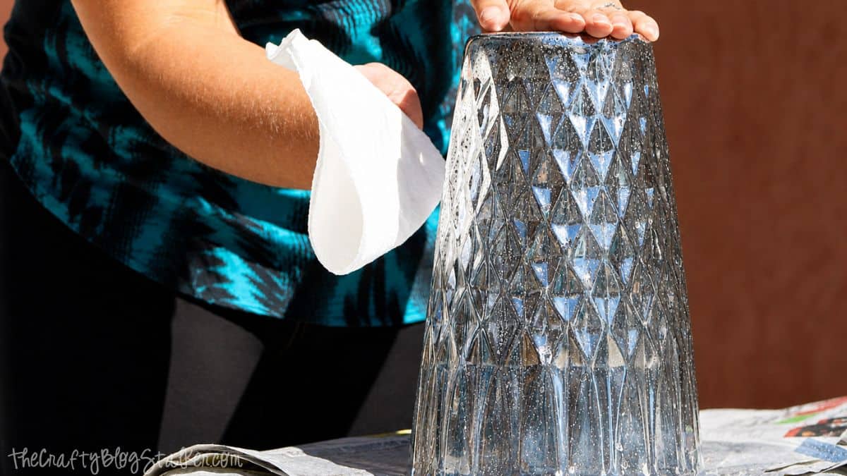 Hand patting a water-speckled glass vase with a paper towel to create a mottled mercury glass finish.