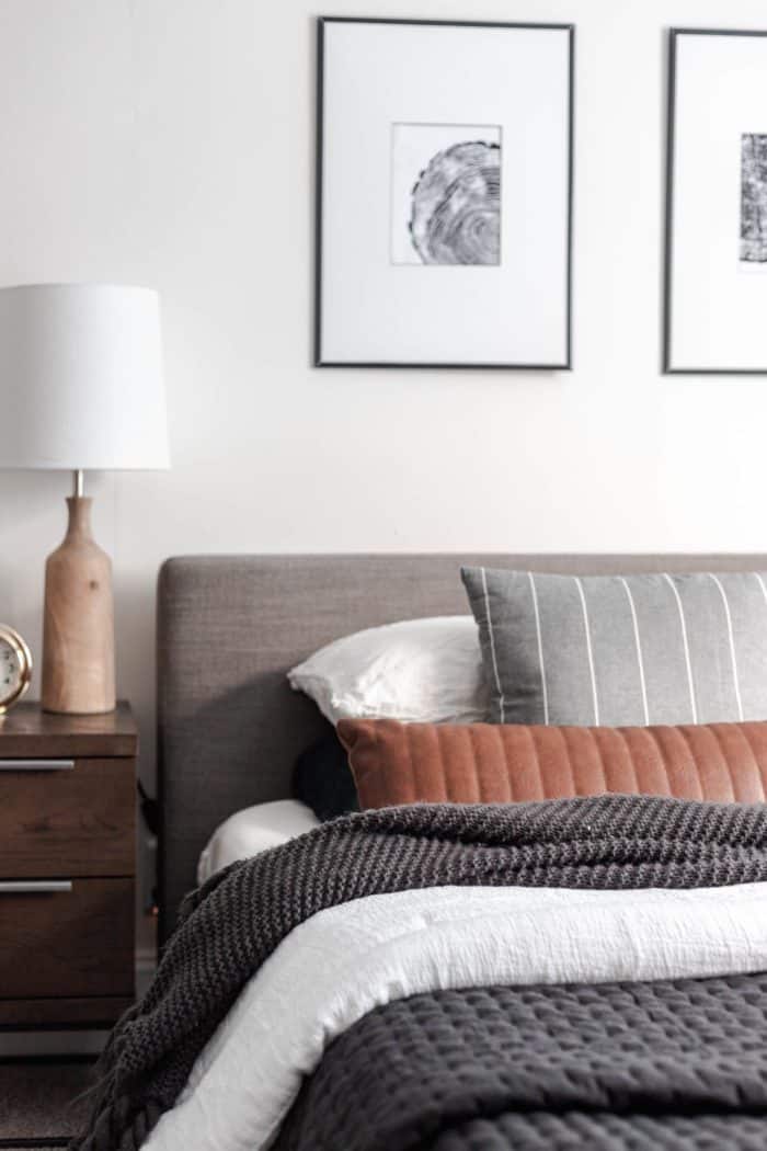 How to Make Your Bed like a Designer - The layered look: Queen size bed with a modern gray headboard, white bedding, dark gray accents and a leather lumbar pillow.