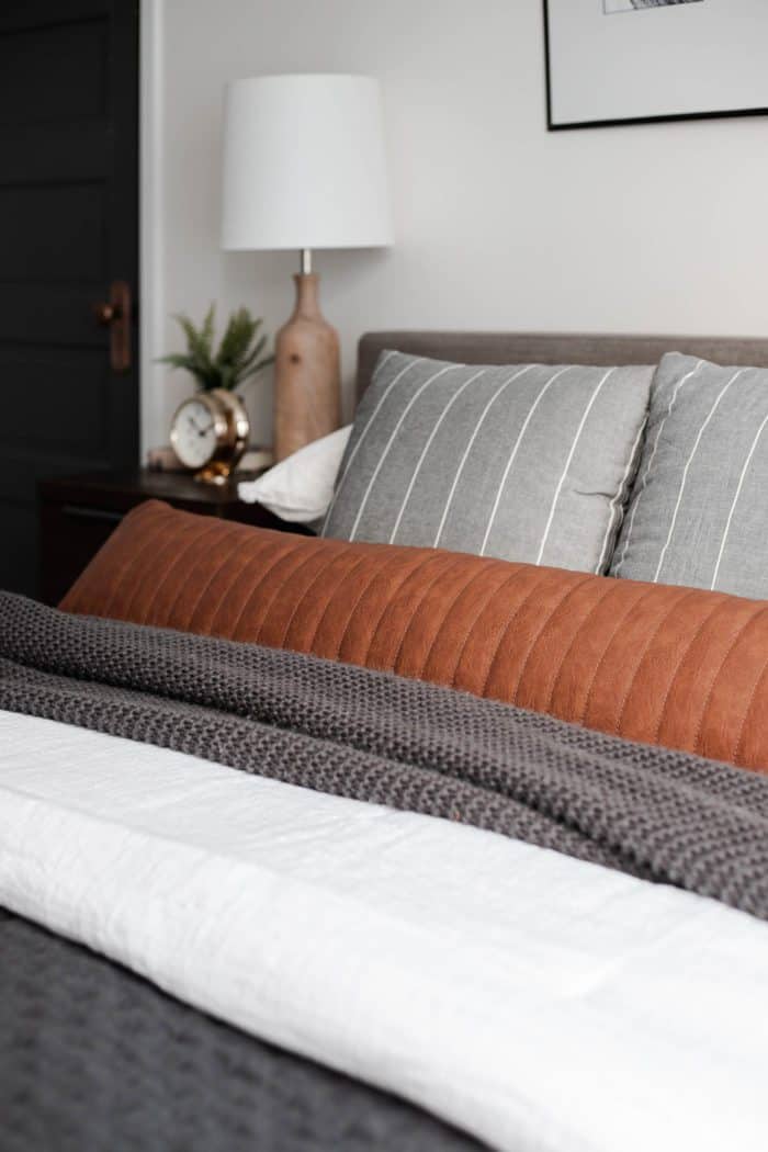 Leather lumbar pillow paired with gray and white striped throw pillows. 