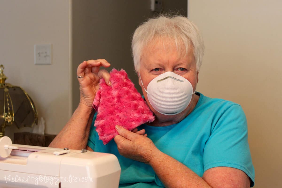 Grandma holding a minky fabric square with a face mask on.