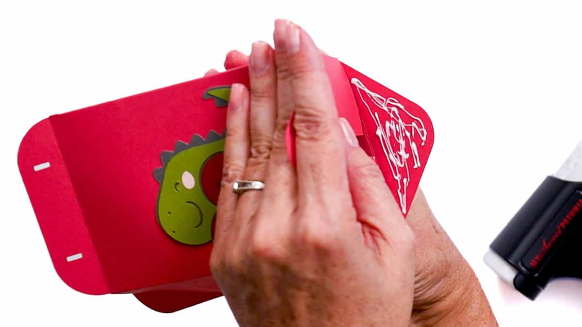 Hands pressing and gluing the bottom flap of a cardstock Valentine treat bag, shaping the bag closed during assembly.