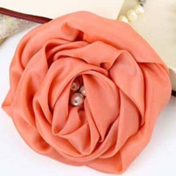 Handmade fabric rose with layered folded petals and small pearl beads in the center, styled as a decorative fabric flower on a flat surface.