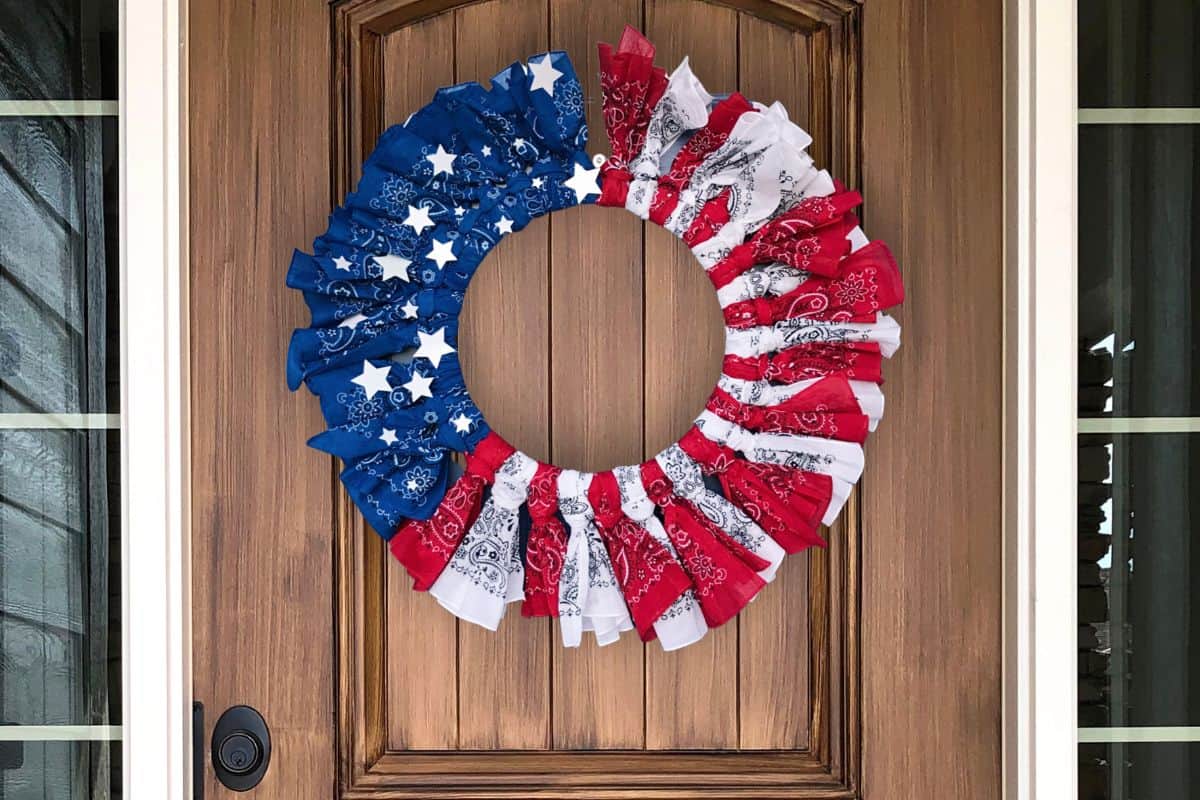 A DIY patriotic bandana wreath hanging on a wood front door.