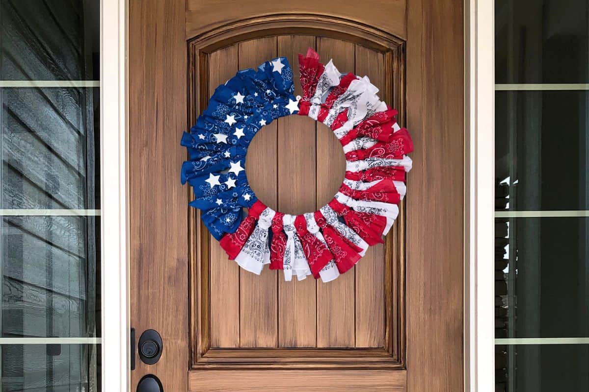 A DIY patriotic bandana wreath hanging on a wood front door.