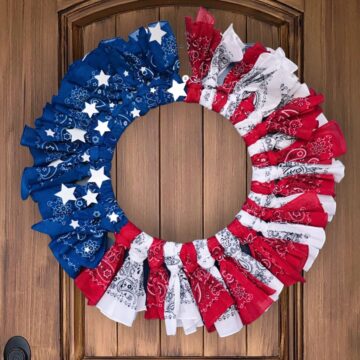 A DIY patriotic bandana wreath hanging on a wood front door.