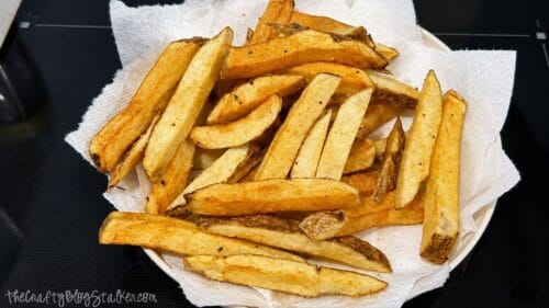 Golden homemade French fries draining on paper towels after frying, with crispy skins and thick-cut potato wedges ready to serve.