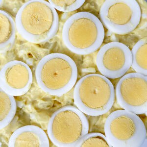 Close-up of classic potato salad topped with neatly arranged slices of hard-boiled eggs in a creamy yellow dressing.