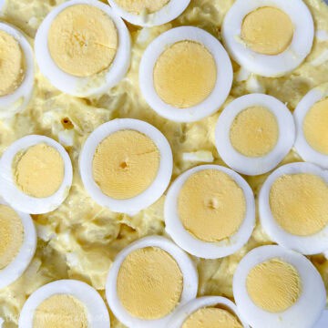 Close-up of classic potato salad topped with neatly arranged slices of hard-boiled eggs in a creamy yellow dressing.