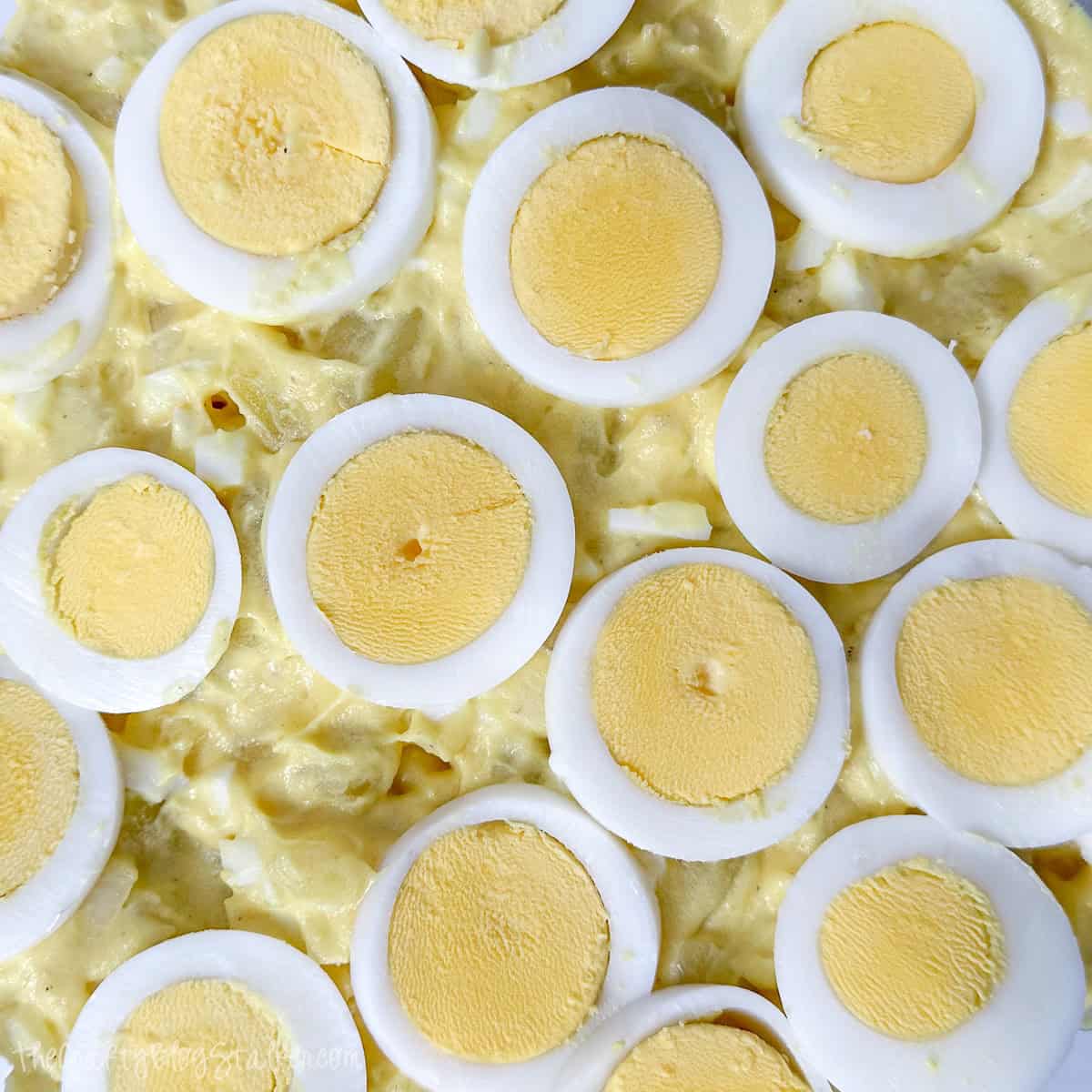 Close-up of classic potato salad topped with neatly arranged slices of hard-boiled eggs in a creamy yellow dressing.