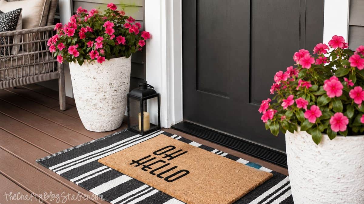 Front porch entry with pink flower planters, a striped outdoor rug, black lantern, and an 