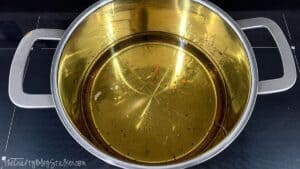 Large stainless steel pot filled with hot cooking oil, ready for frying homemade potato fries on a stovetop.