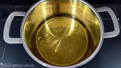 Large stainless steel pot filled with hot cooking oil, ready for frying homemade potato fries on a stovetop.