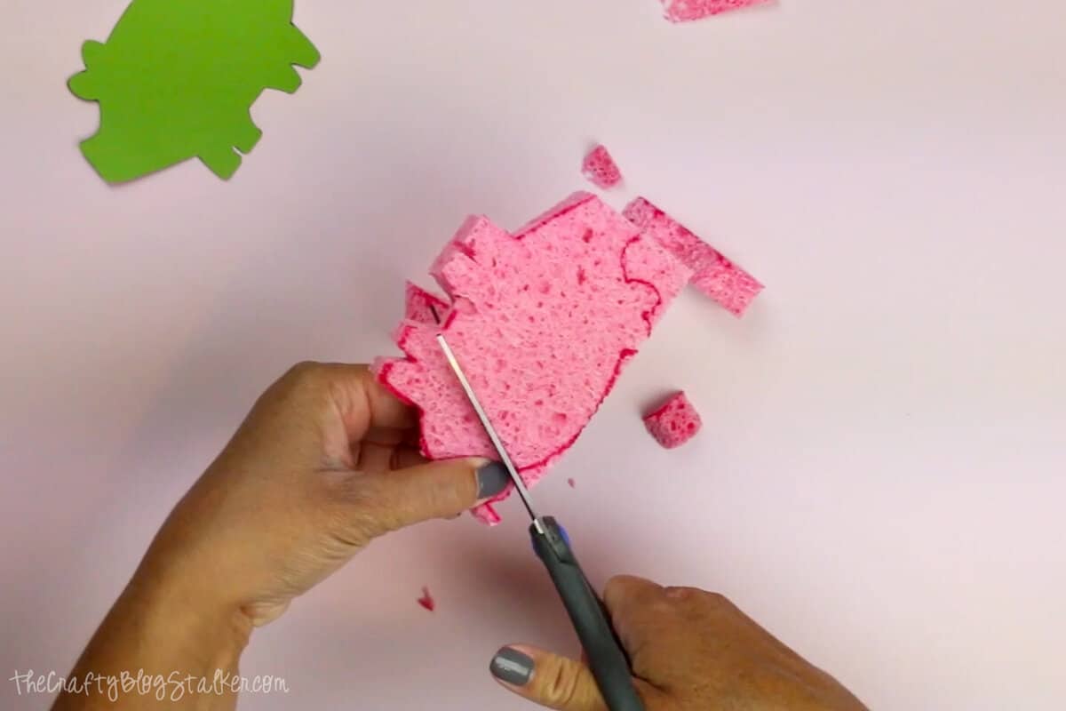 Hands cutting a sponge with a pair of scissors.