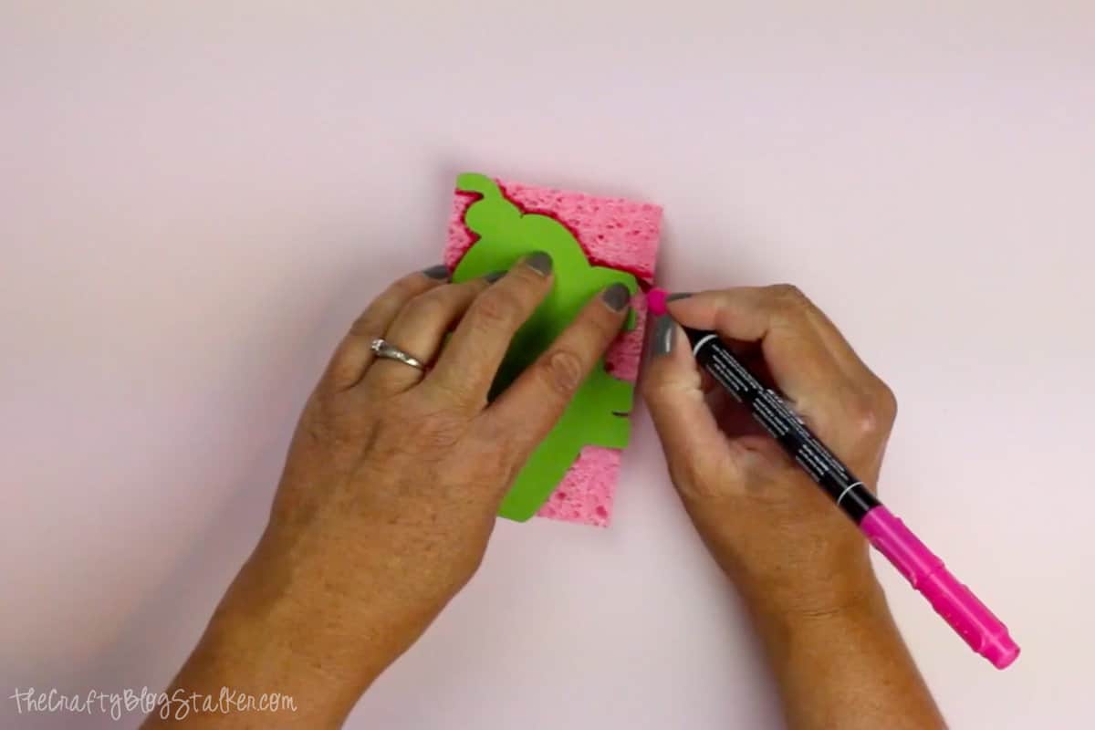 Hands tracing a pig shape onto a sponge with a marker.