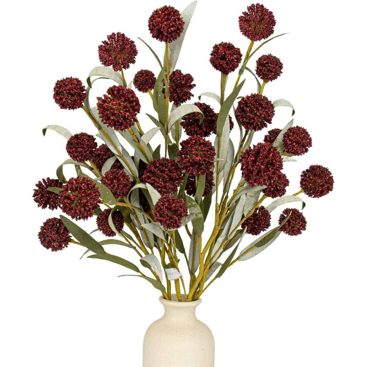 Artificial fall flower arrangement with burgundy pom-pom blooms and muted green leaves displayed in a cream vase.