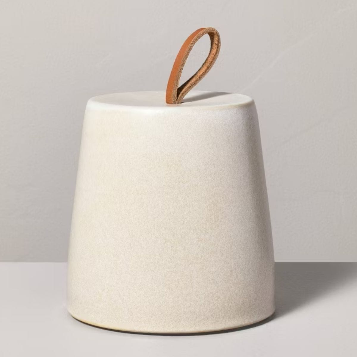 White ceramic door stopper with a tapered shape and brown leather loop handle, displayed against a neutral background.