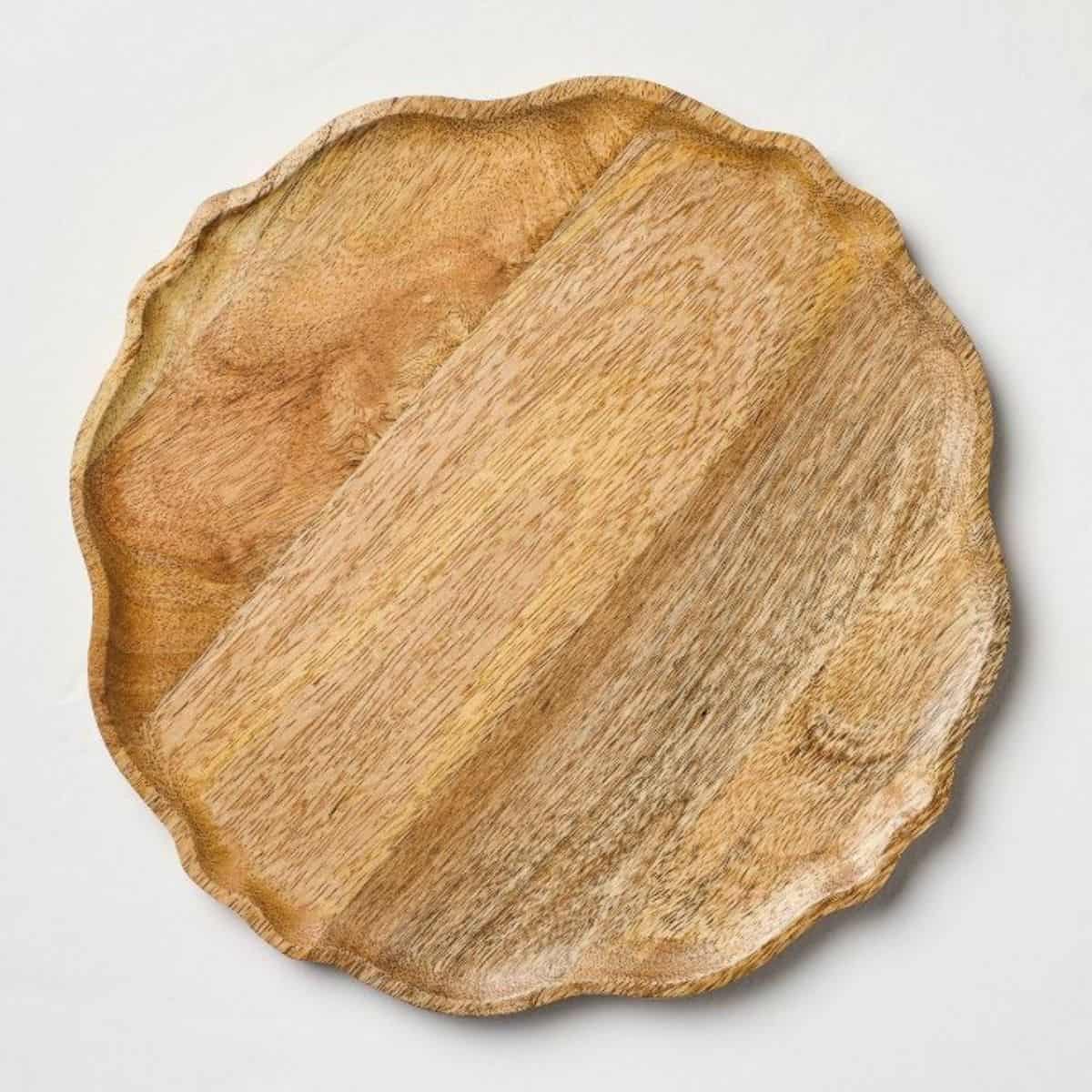 Round wooden charger plate with natural wood grain and a softly scalloped, irregular raised edge.