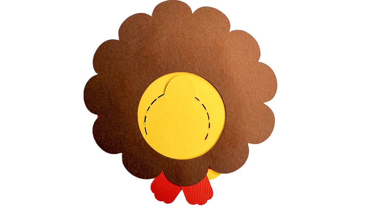 Back of a cardstock turkey treat holder showing brown feathers, orange feet, and a yellow perforated flap for accessing the candy.