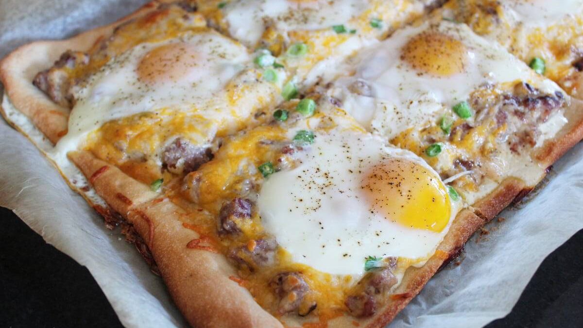 Sheet pan breakfast pizza topped with melted cheese, sausage, and sunny-side-up eggs.