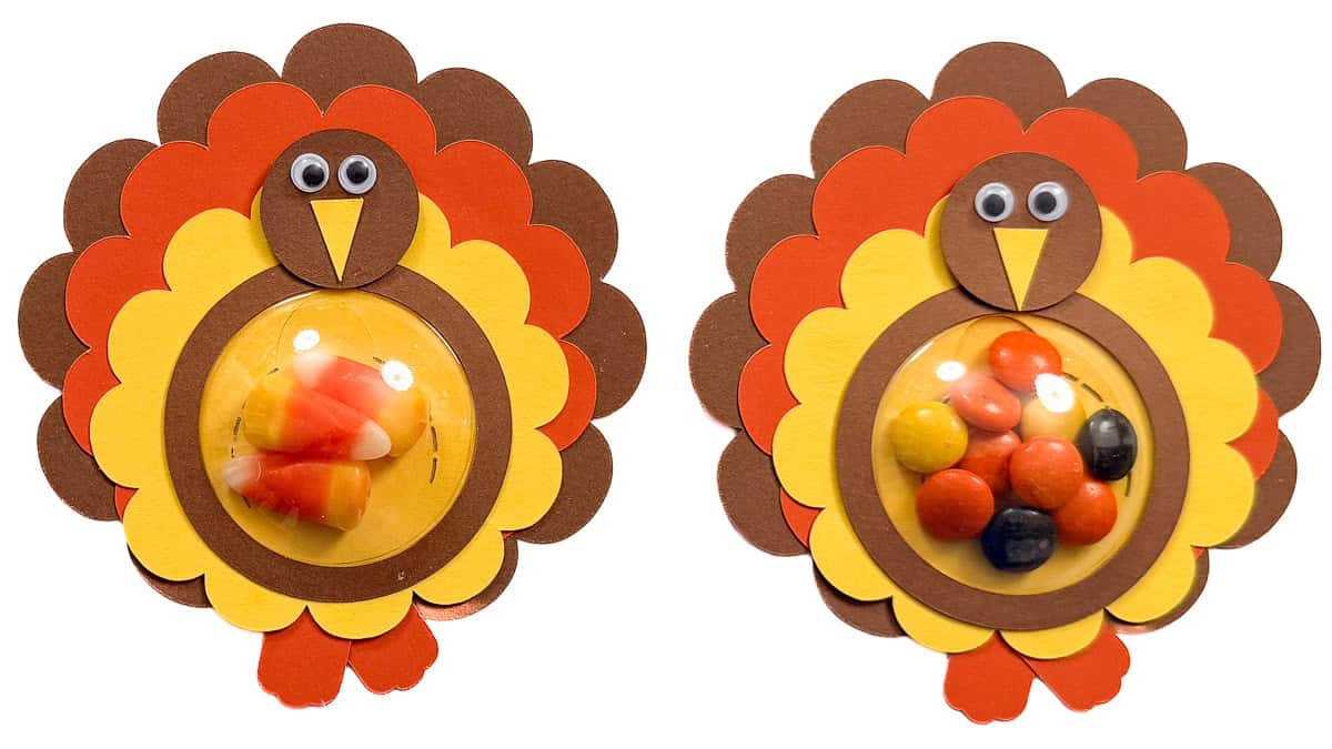 Two paper turkey treat holders with googly eyes and clear domes filled with candy corn and colorful candies.