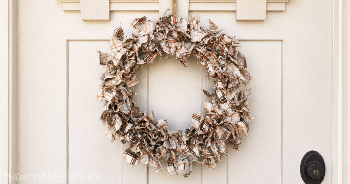 DIY fabric wreath made from plaid fabric strips hanging on a white front door, creating a cozy rustic fall decoration.