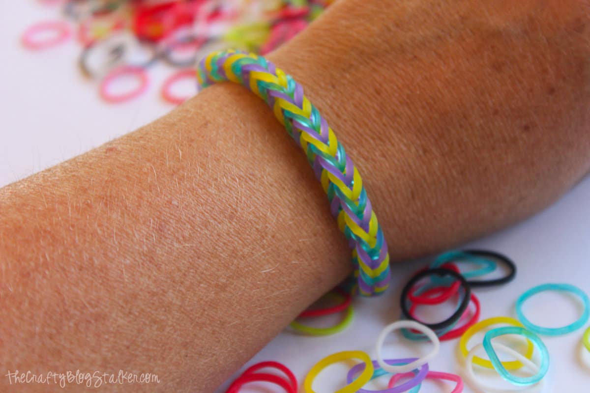 A wrist wearing a fishtail bracelet in yellow, purple and blue.